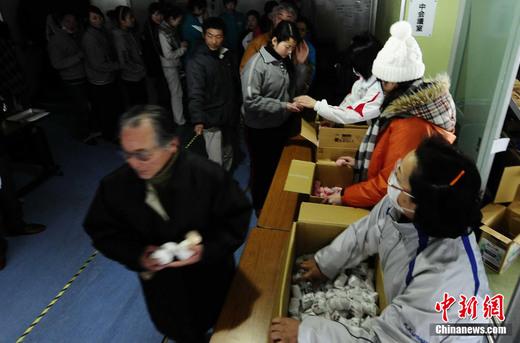 3月16日，在日本岩手县大船渡地区公民会馆避难的民众排队领取食物。中新社发 侯宇 摄